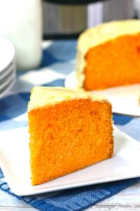Slice of Instant Pot orange cake on white plate with rest of cake in background