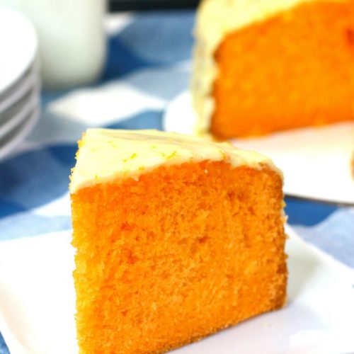 Slice of Instant Pot orange cake on white plate with rest of cake in background