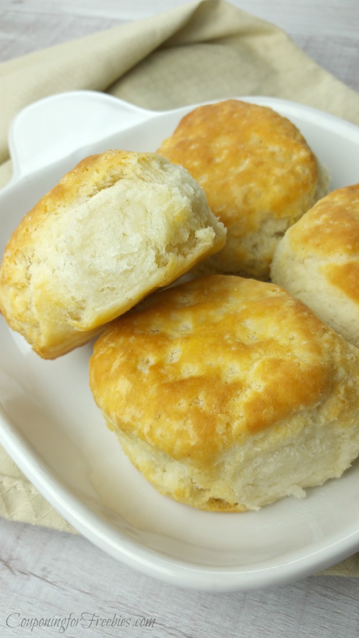 Four fresh baked golden biscuits on white plate setting on tan cloth napkin